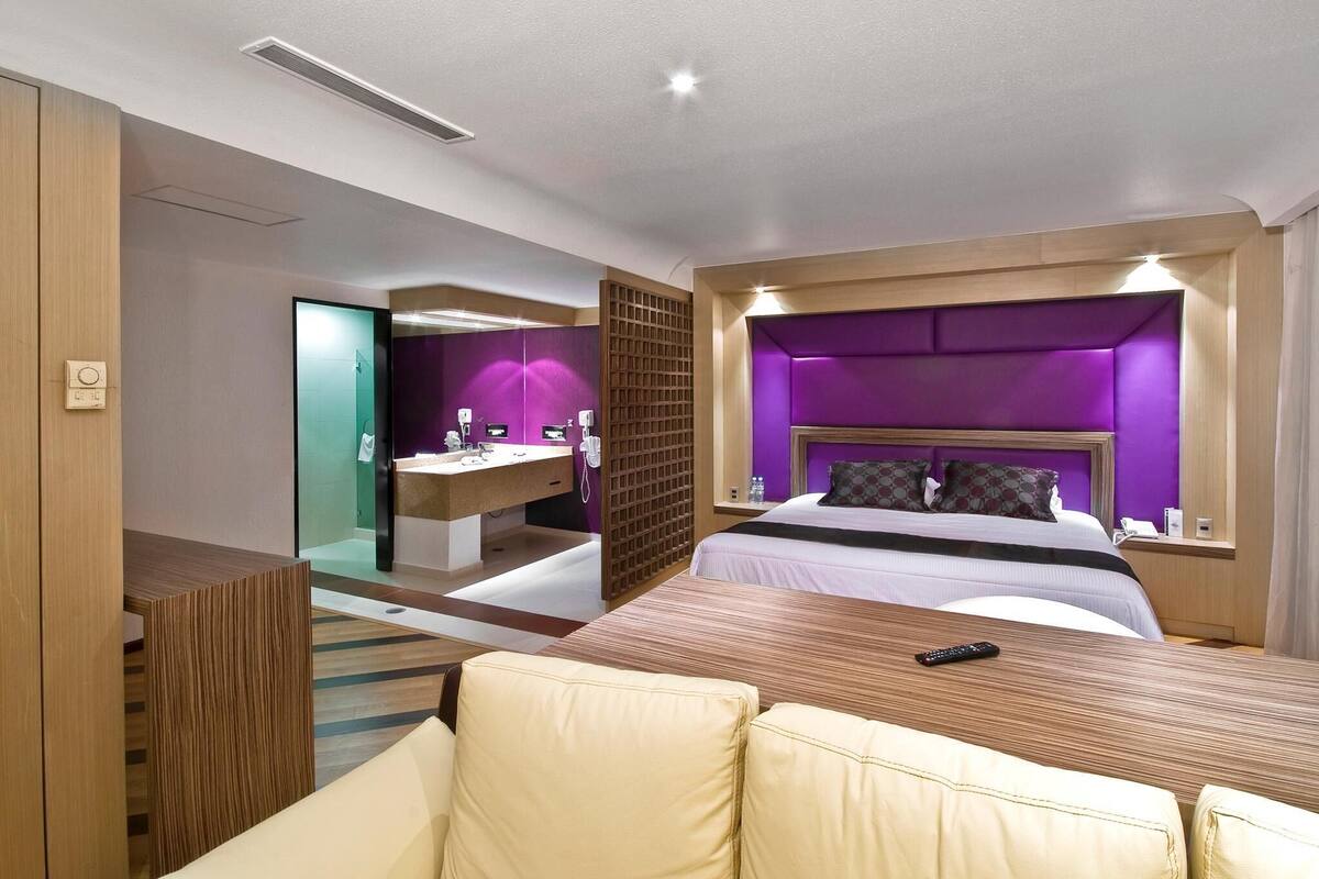 A hotel room with a bed, a desk, a mirror, and a bathroom visible through an open door.