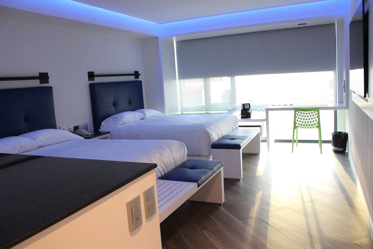 A modern hotel room with two beds, a desk, and a view of the city.