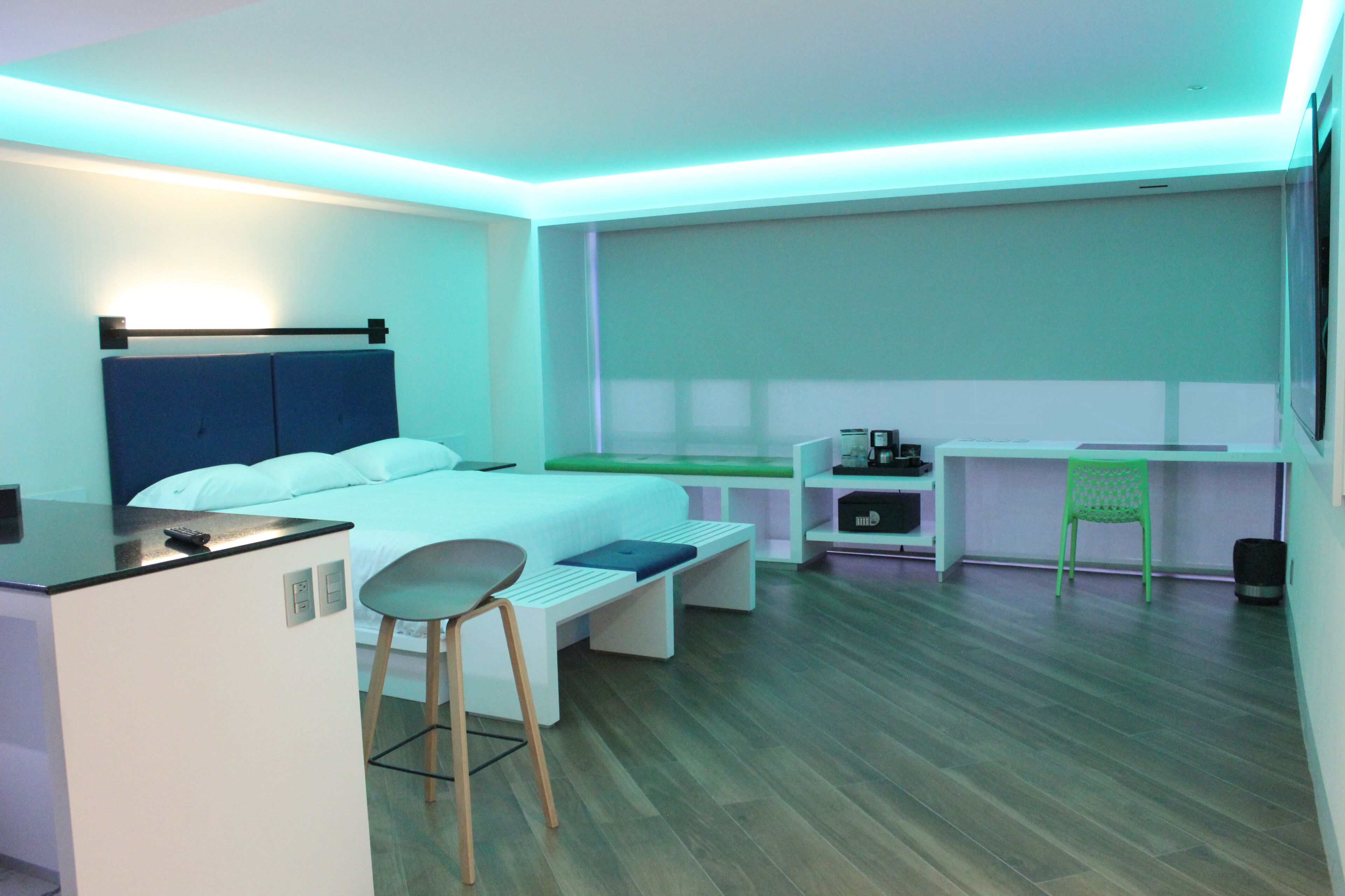 A modern hotel room with a bed, a desk, a chair, and a small kitchenette.