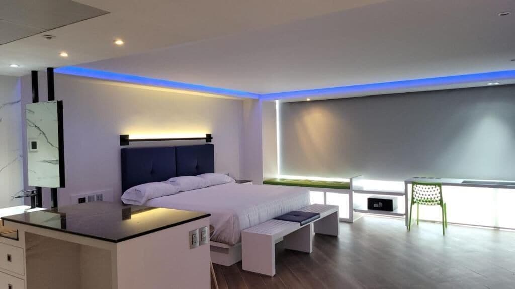 Un dormitorio moderno con cama, mesita de noche, banco y un escritorio con silla.
