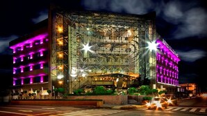 A modern building with a glass facade and a metal framework, illuminated by purple lights.