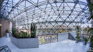 A spacious atrium with a glass ceiling, featuring a central garden area with potted plants and a metal railing.