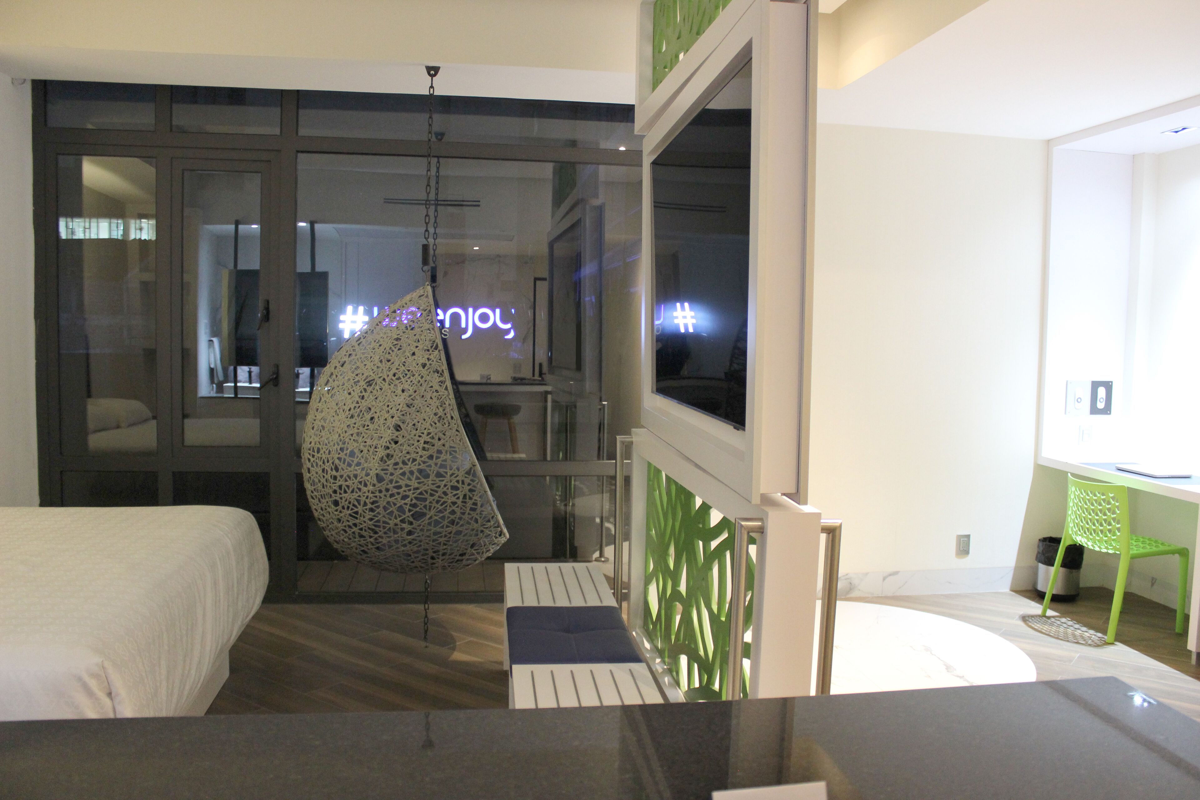 A modern hotel room with a bed, a hanging chair, a desk, and a view of the city.
