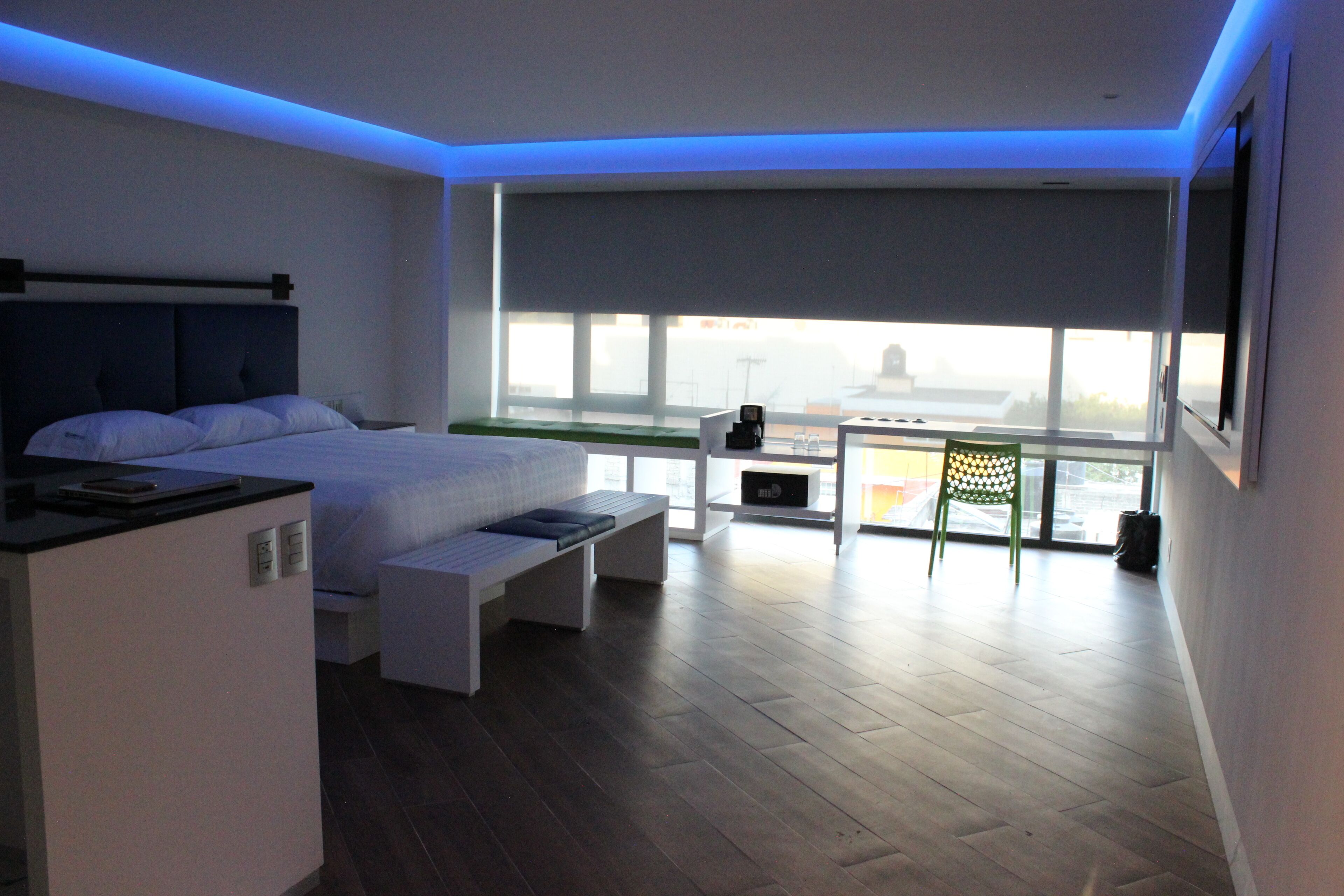 Un dormitorio moderno con cama, mesita de noche y vistas a la ciudad a través de amplias ventanas.