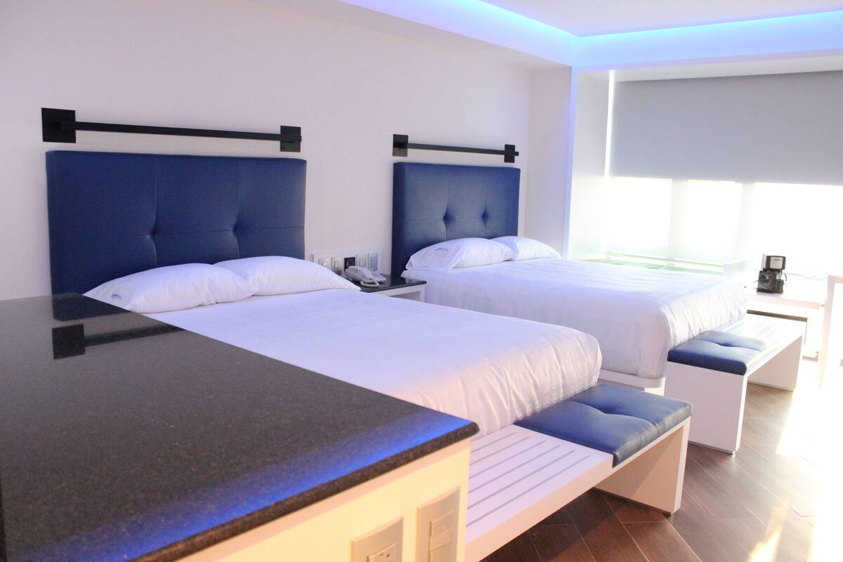 A hotel room with two beds, a desk, and a bench.
