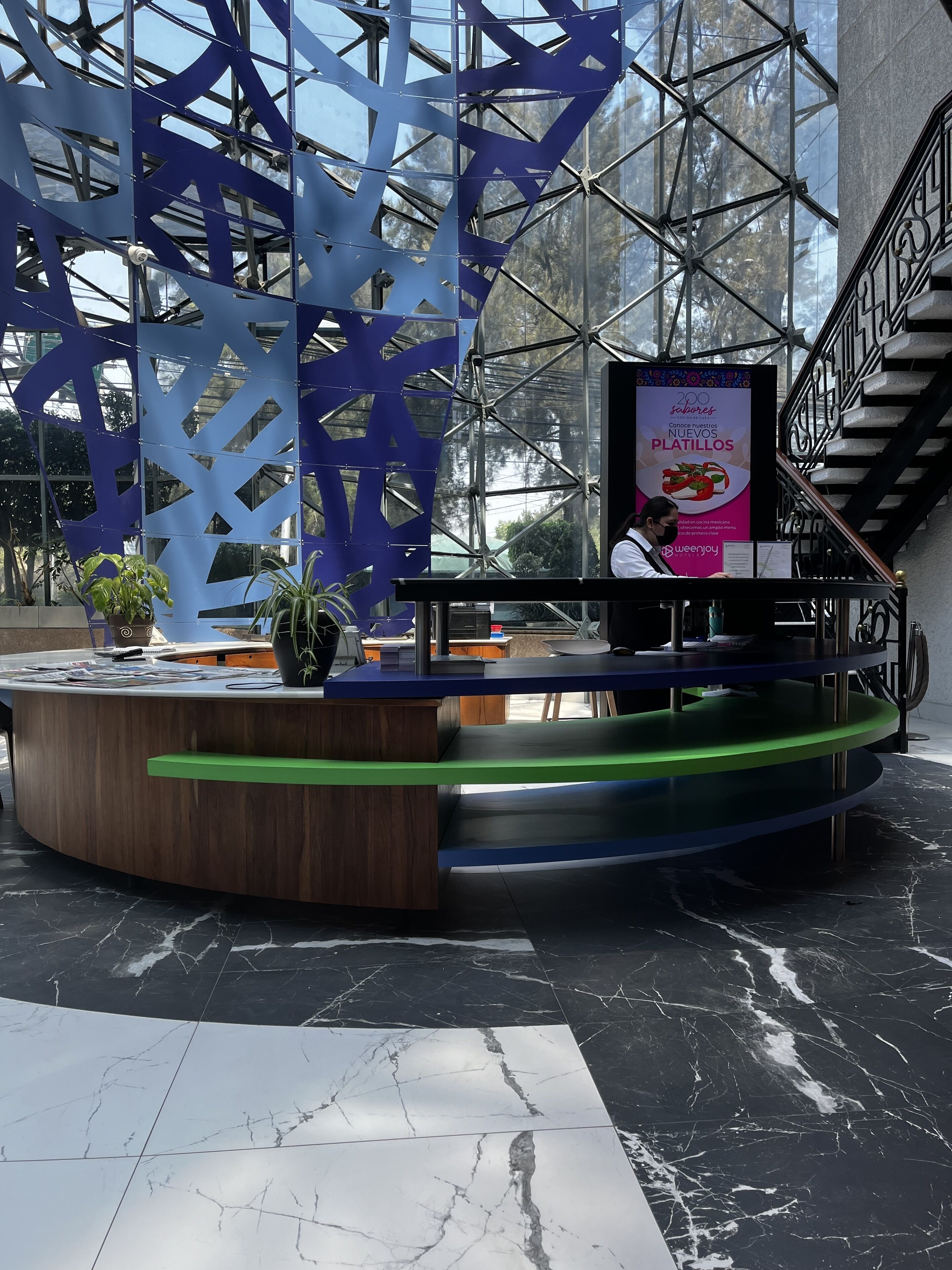 A modern reception area with a wooden counter, a blue and green decorative structure, and a sign advertising new platillos.