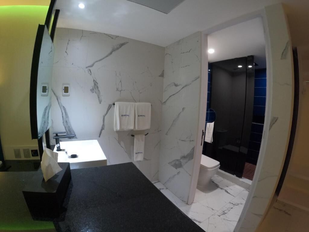 A modern bathroom with a marble wall, a black countertop, a white sink, and a separate shower area.
