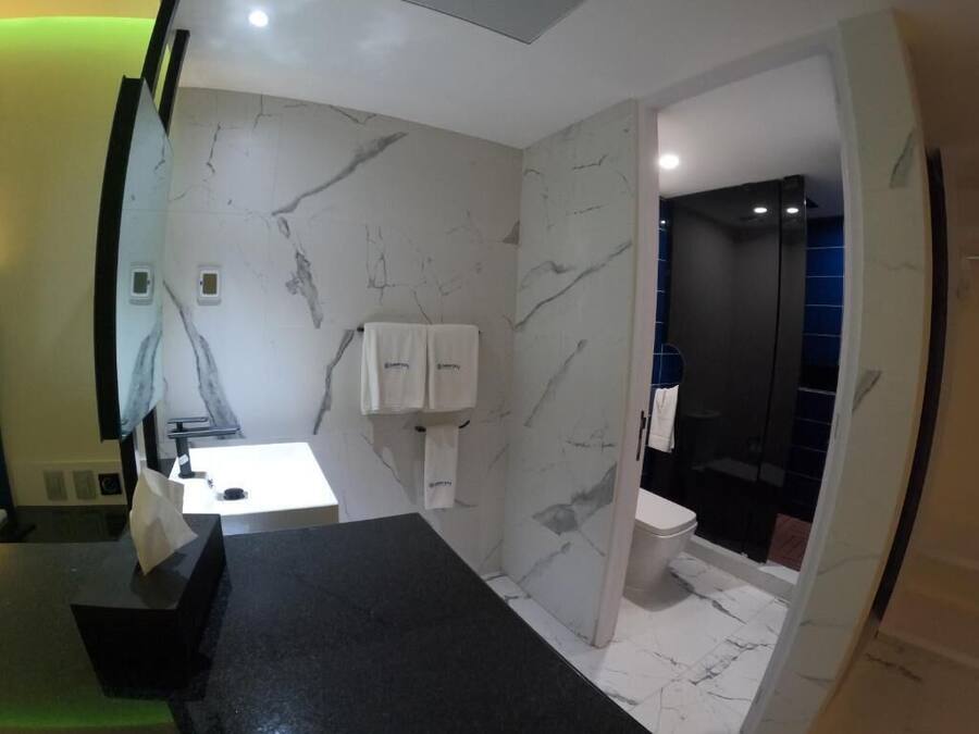 A modern bathroom with a marble wall, a black countertop, a white sink, and a separate shower area.