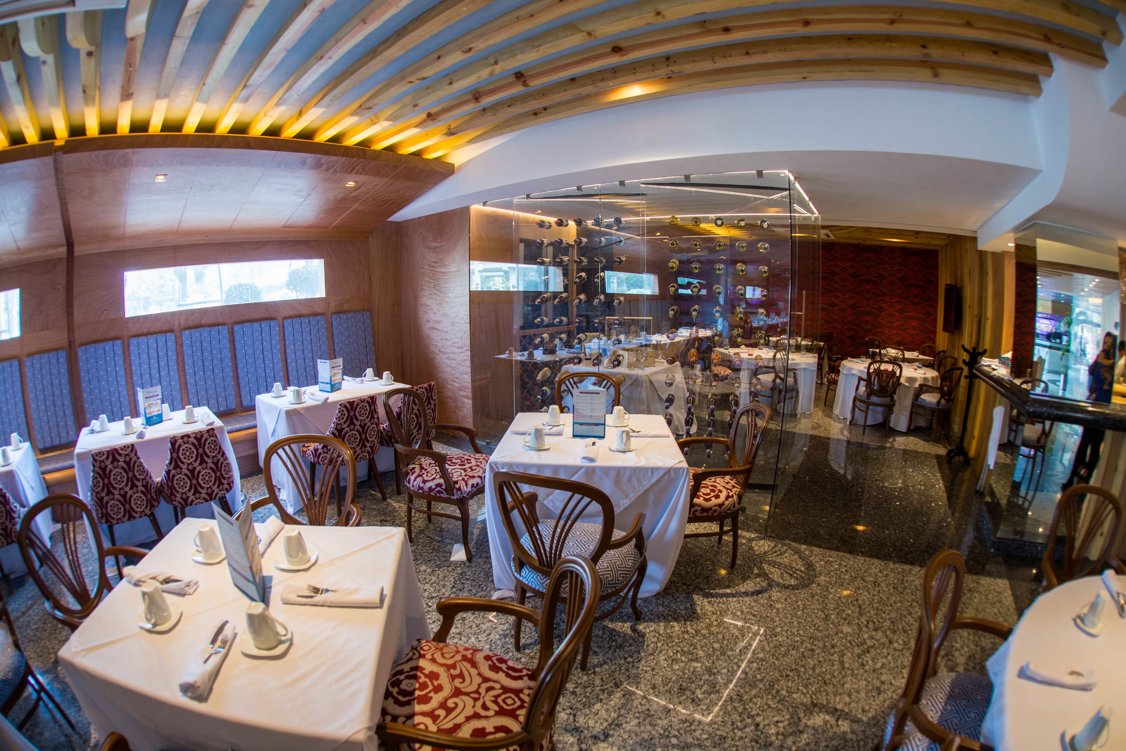 A restaurant with round tables, wooden chairs, and a curved ceiling.