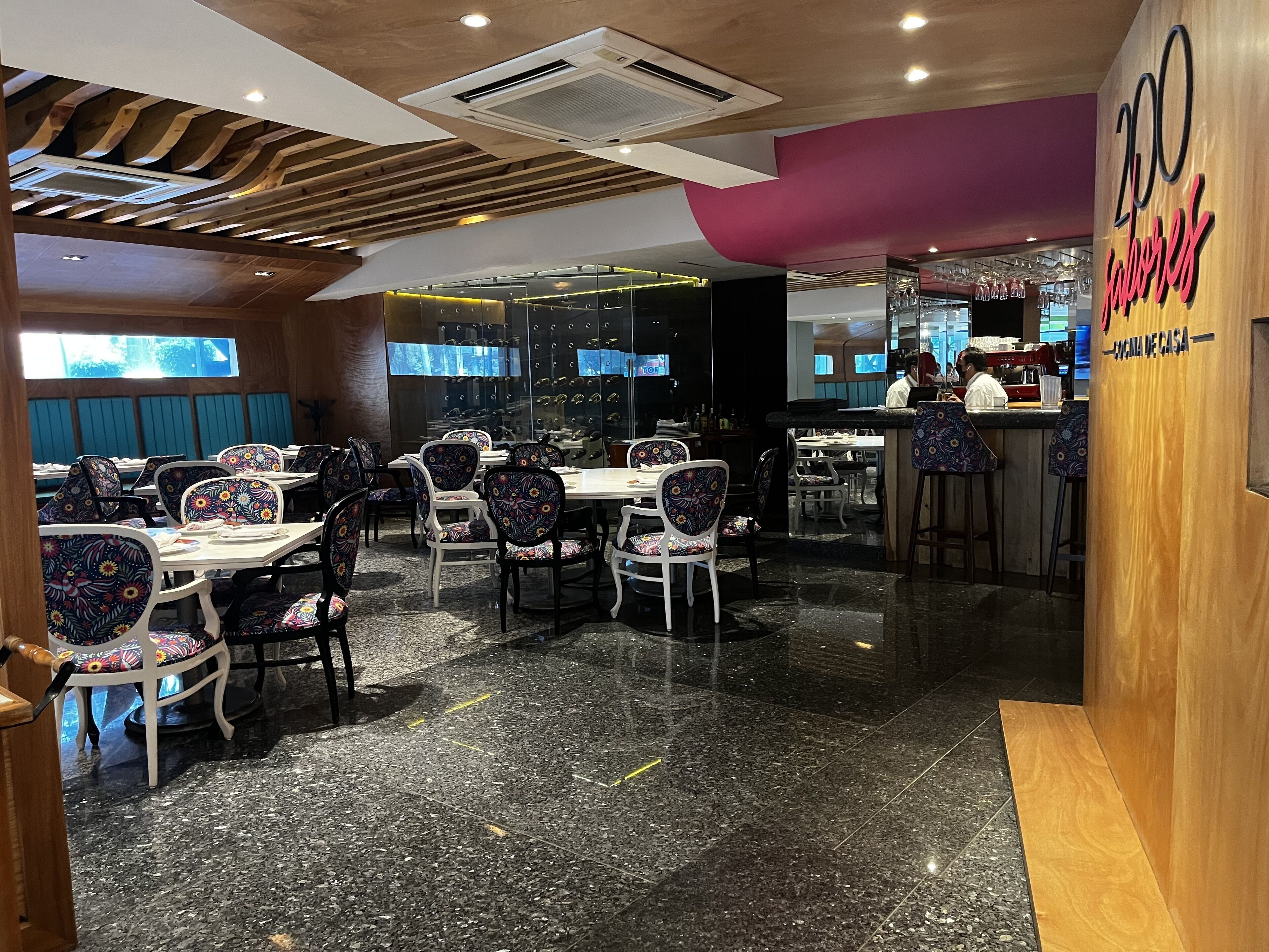Interior de restaurante con mesas y sillas, una zona de bar y una pared decorativa de madera.