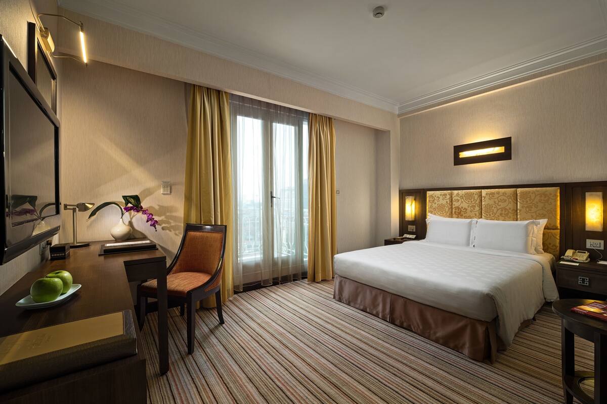 Una habitación de hotel con una cama, un escritorio con una silla, una lámpara y una mesita de noche.