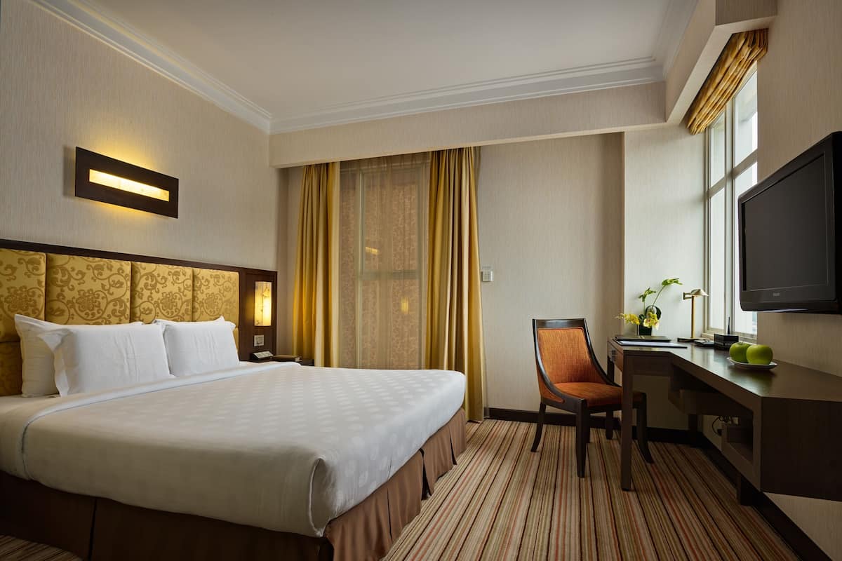 Habitación de hotel con una cama grande, un escritorio con silla, televisor y ventana con cortinas.