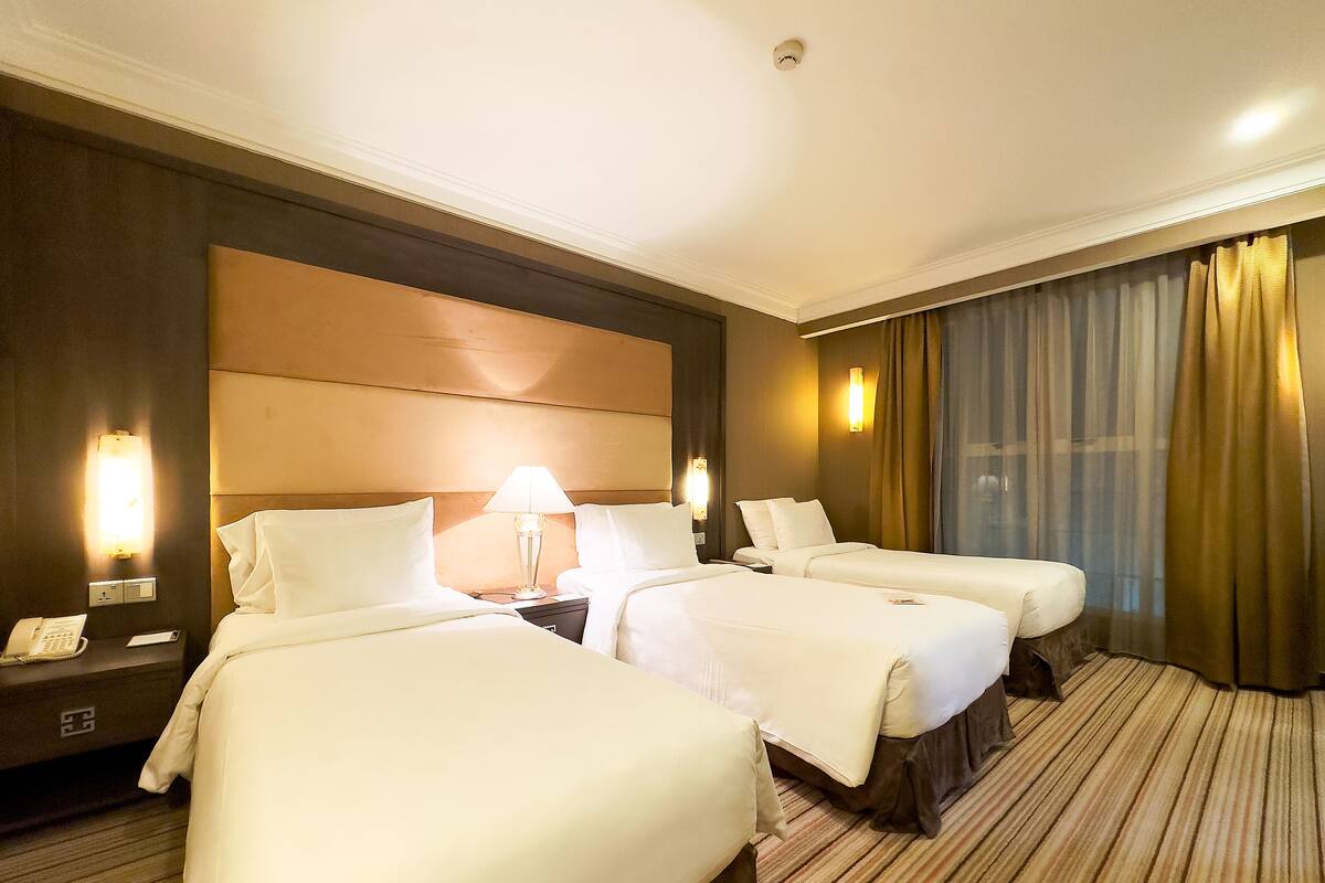 Habitación de hotel con dos camas, una mesita de noche con teléfono y una lámpara de pared.
