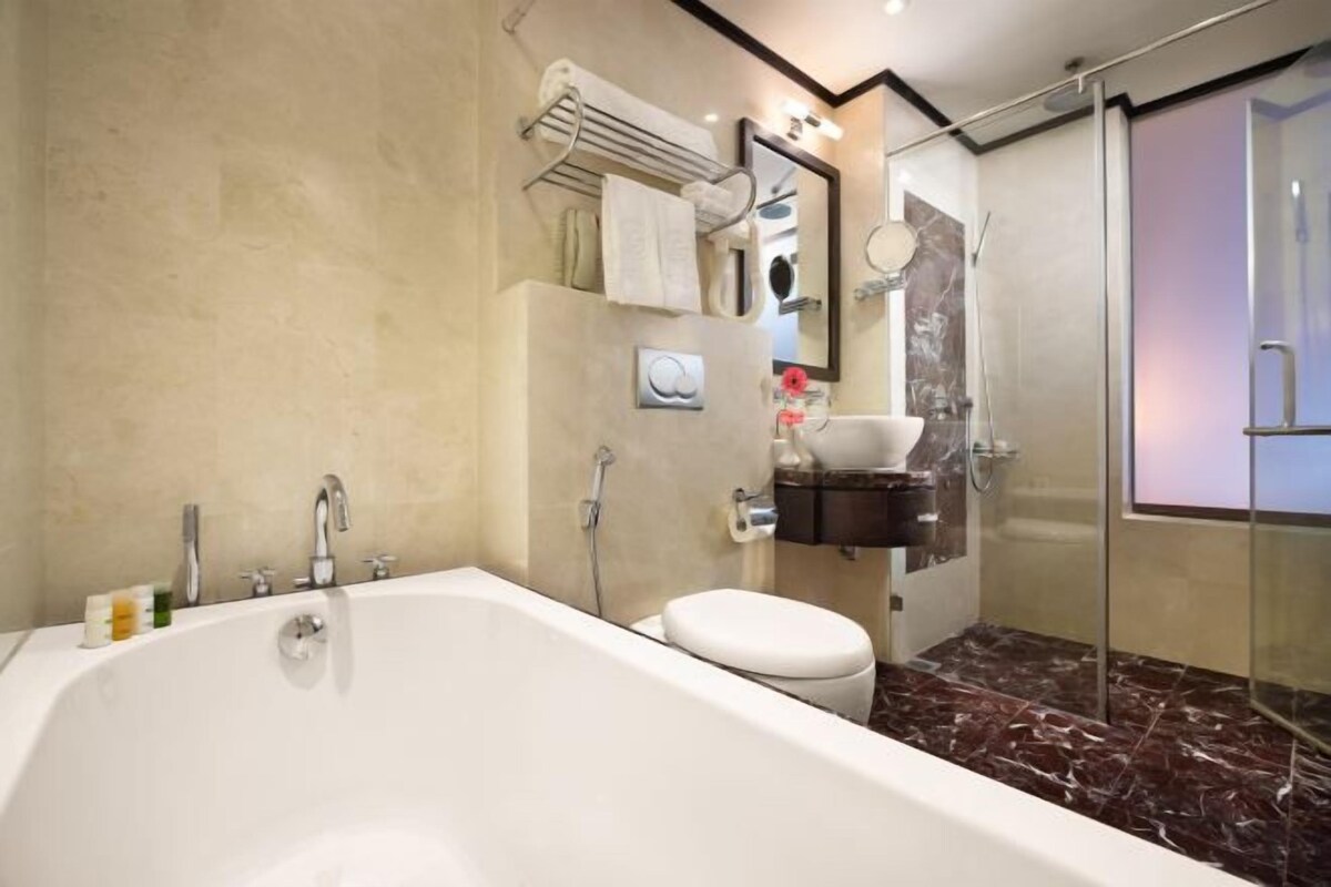 A modern bathroom with a large bathtub, a toilet, and a glass-enclosed shower area.