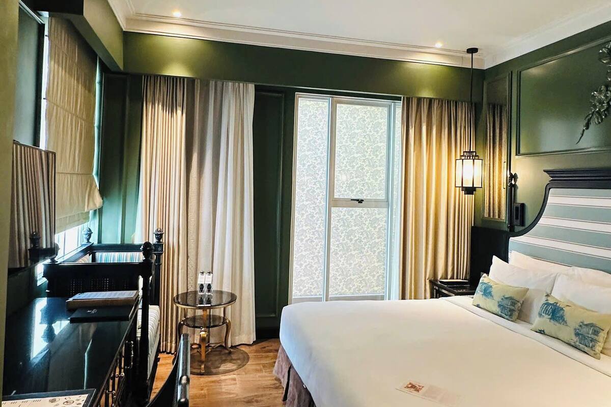 Habitación de hotel con una cama grande, un escritorio, una silla, una mesita y una ventana con cortinas.