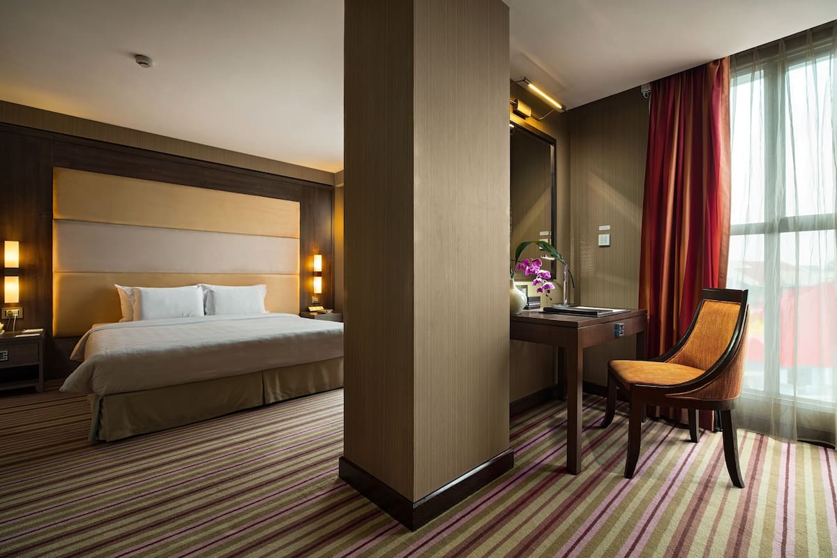 Una habitación de hotel con una cama grande, un escritorio, una silla y un ventanal con cortinas.