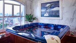 Une salle de bain moderne avec une grande baignoire, un banc en bois, des plantes en pot et une vue sur la ville grâce à de grandes fenêtres.