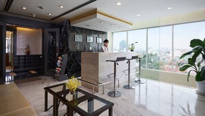 Un hall d’hôtel moderne doté d’un comptoir d’accueil, d’un espace salon et de grandes fenêtres offrant une vue sur la ville.