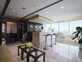 A modern hotel lobby with a reception desk, seating area, and large windows offering city views.