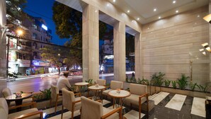 Un hall d’hôtel moderne avec un sol en marbre, des sièges confortables et de grandes fenêtres donnant sur une rue animée.