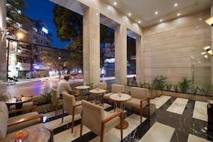 A modern hotel lobby with a marble floor, comfortable seating, and large windows overlooking a busy street.