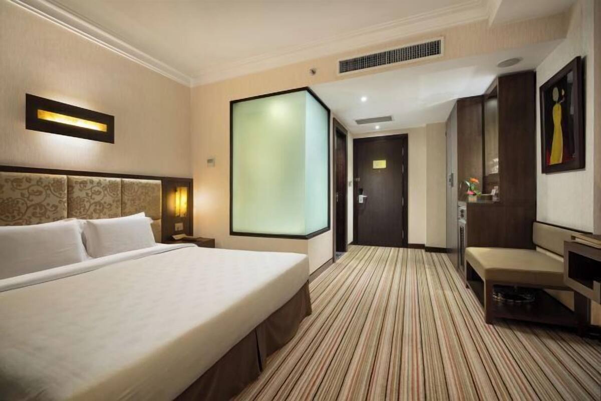 Habitación de hotel con una cama grande, un escritorio, una silla, un espejo y una puerta que conduce a otra habitación.