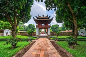 A traditional Chinese pavilion with a tiled pathway leading to it, surrounded by lush greenery and stone walls.