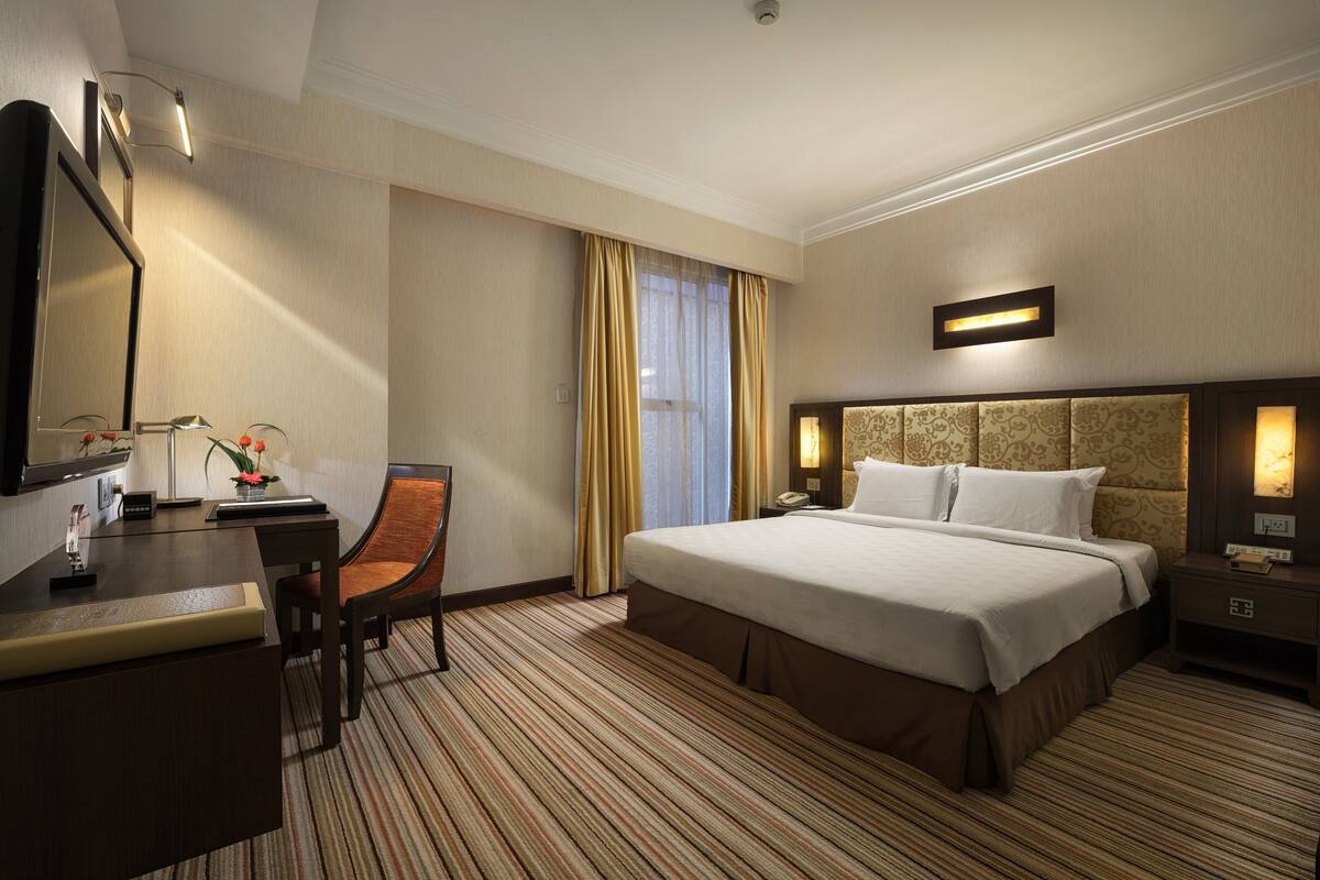 Habitación de hotel con cama, escritorio, silla y un ventanal con cortinas.