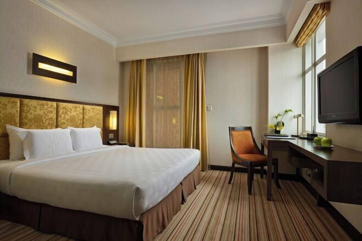 Habitación de hotel con una cama grande, un escritorio con silla, televisión y ventana con cortinas.