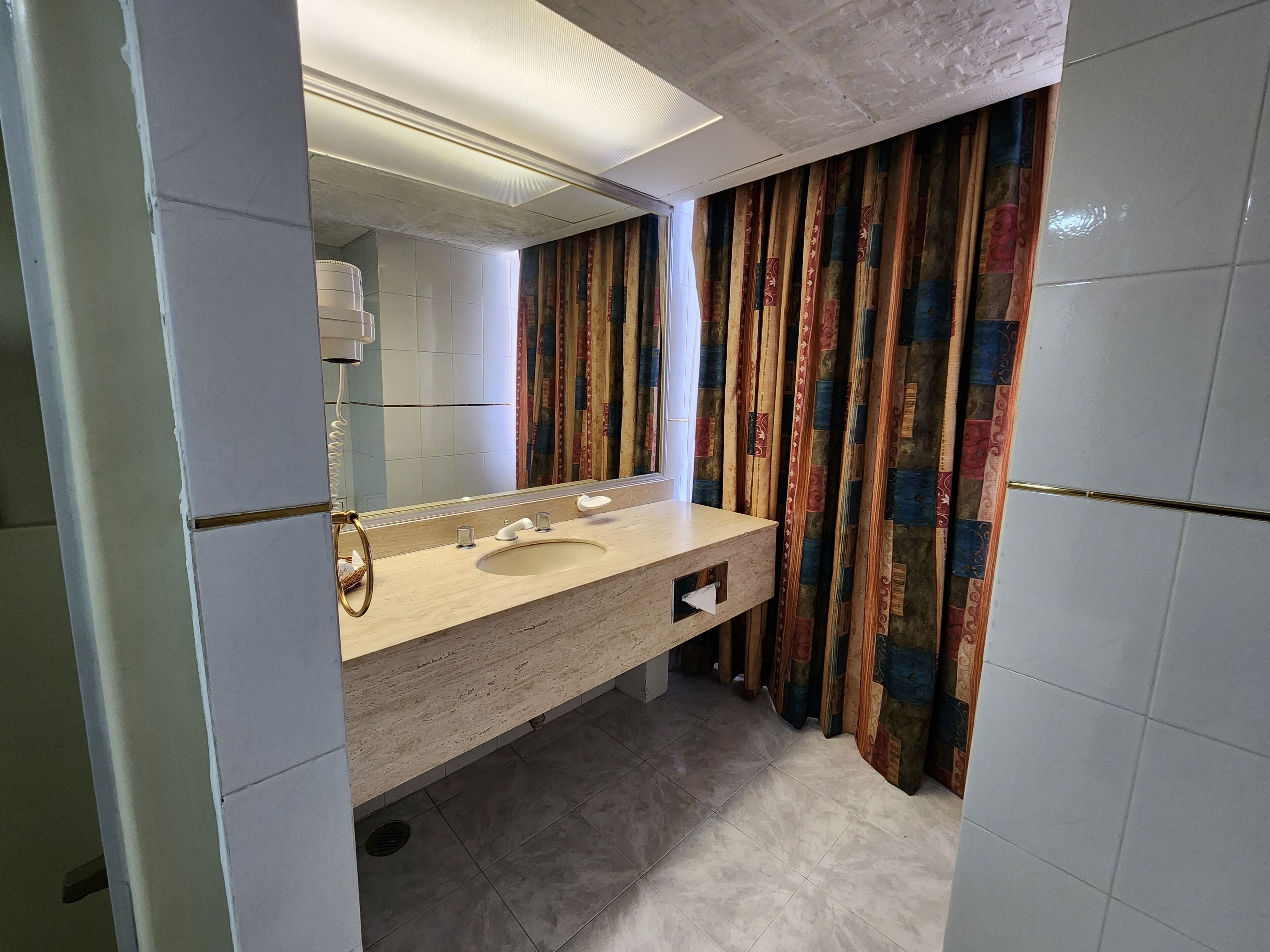 Un baño con un lavamanos color beige, un espejo y una cortina de ducha con un estampado colorido.
