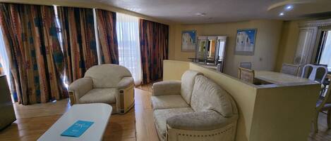 A living room with a sofa, armchair, and a small table with a menu. There is a kitchen area with a counter and chairs.