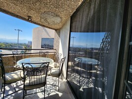 Un balcon avec une table et des chaises en verre, un mur en pierre et une vue sur le paysage urbain.