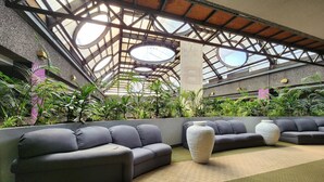 Um espaço moderno e interno com teto alto, plantas verdes e sofás cinzentos.