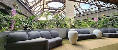 Un espacio interior moderno con techo alto, plantas verdes y sofás grises.