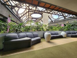 Un espace intérieur moderne, doté d’un haut plafond, de plantes vertes et de canapés gris.