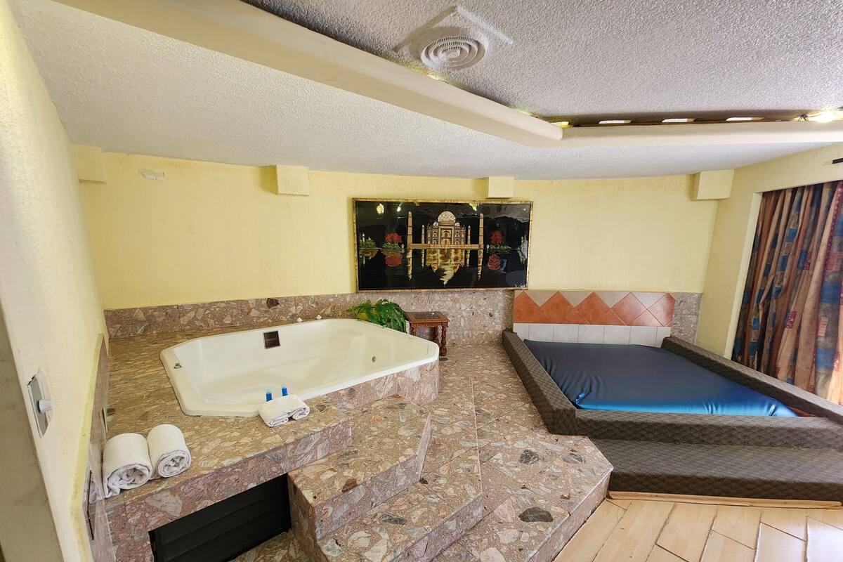 A bathroom with a bathtub, a shower, and a toilet. There is a painting on the wall and a window with curtains.