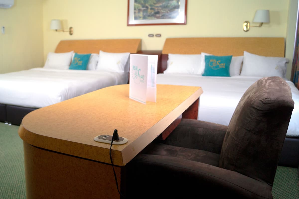 A hotel room with two beds, a desk with a laptop, and a chair.