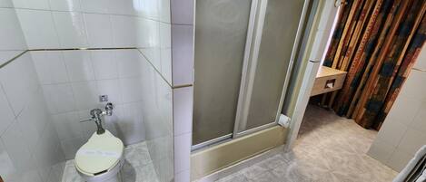A bathroom with a toilet, a trash bin, and a shower area.