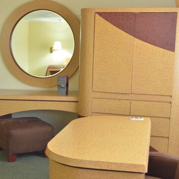 A hotel room with a wooden desk, a round mirror, a brown ottoman, and a green box on the desk.