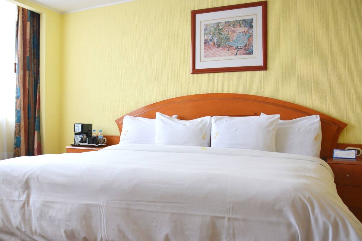 A hotel room with a large bed, a nightstand with a coffee maker, and a framed picture on the wall.