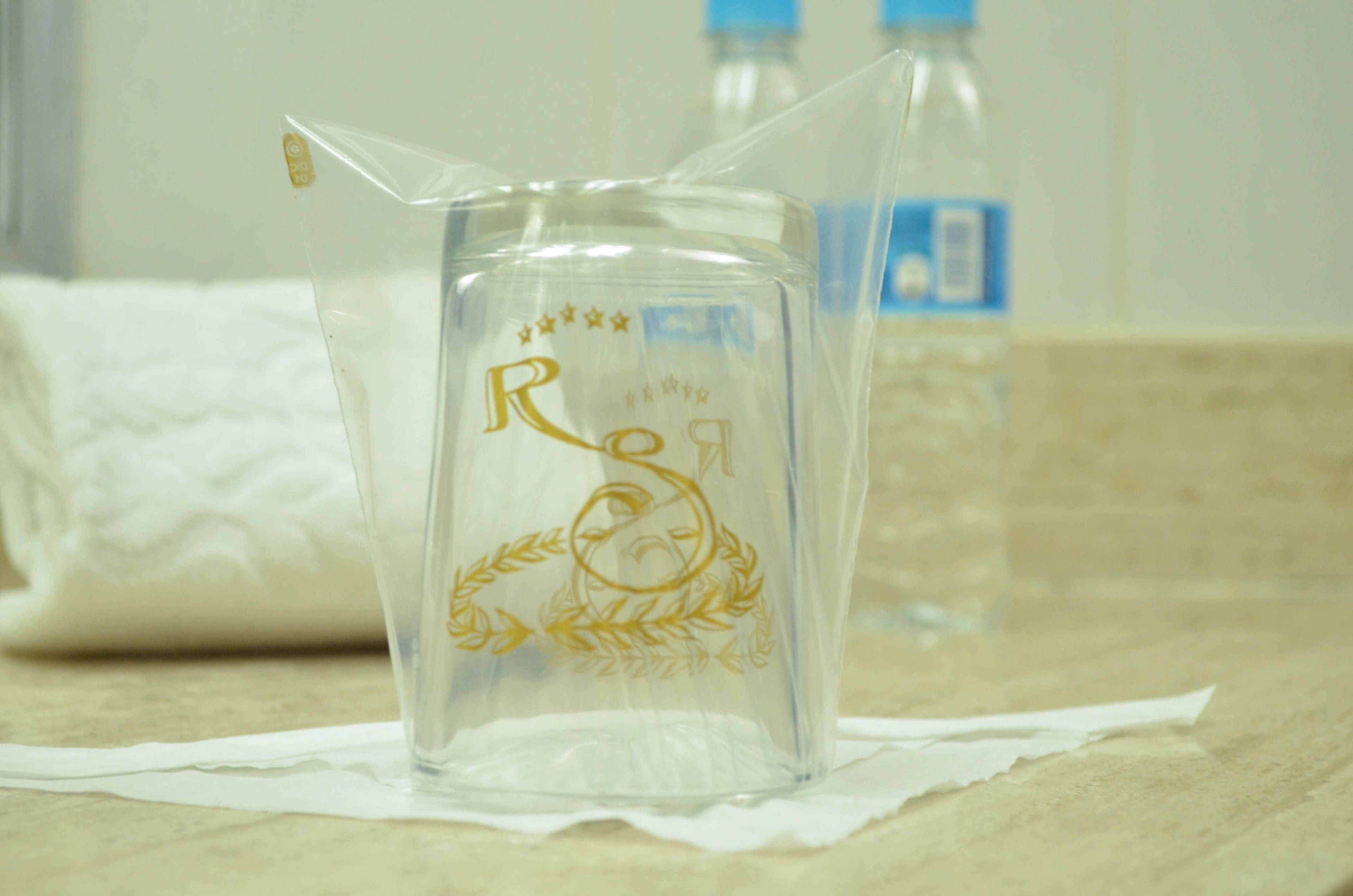 A clear glass pitcher with embossed text and a laurel wreath design on a countertop.