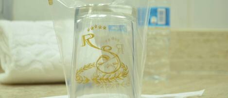 A clear glass pitcher with embossed text and a laurel wreath design on a countertop.