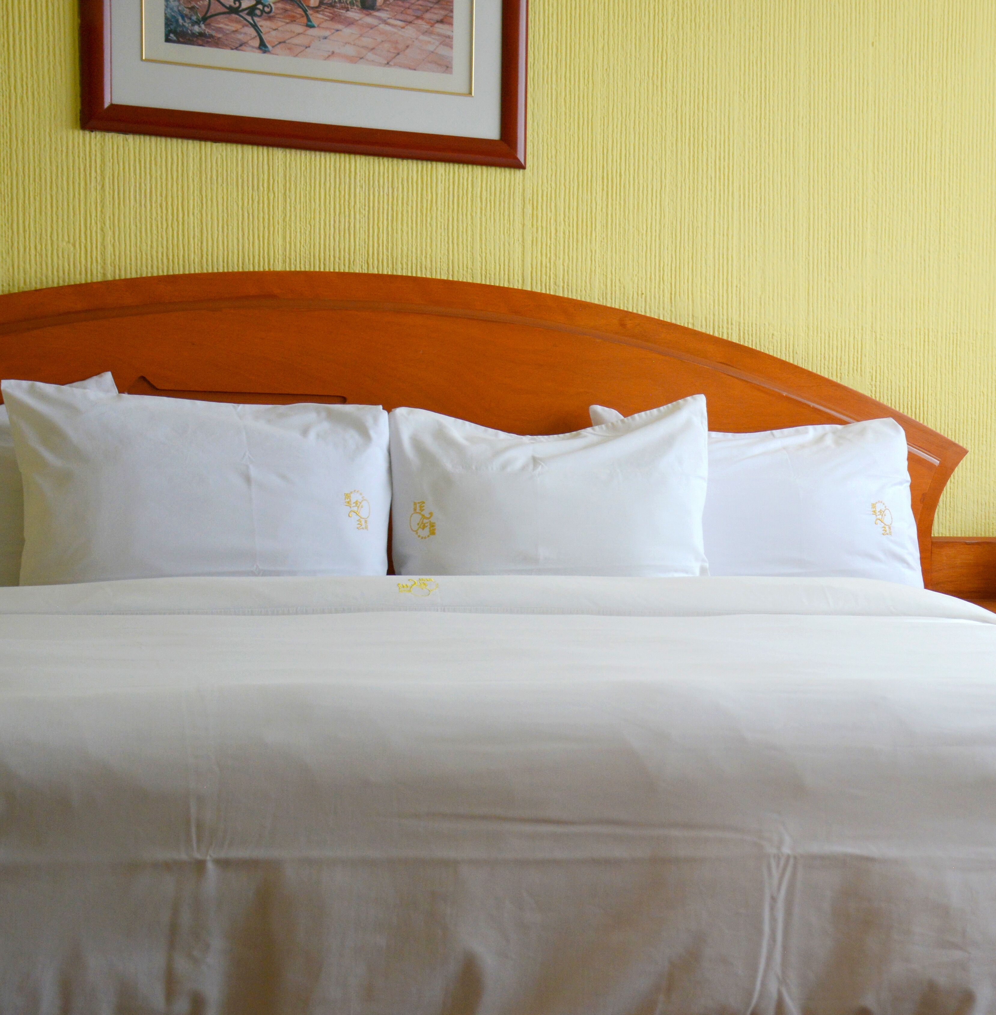 A neatly made bed with white linens and pillows, a wooden headboard, and a framed picture on the wall.