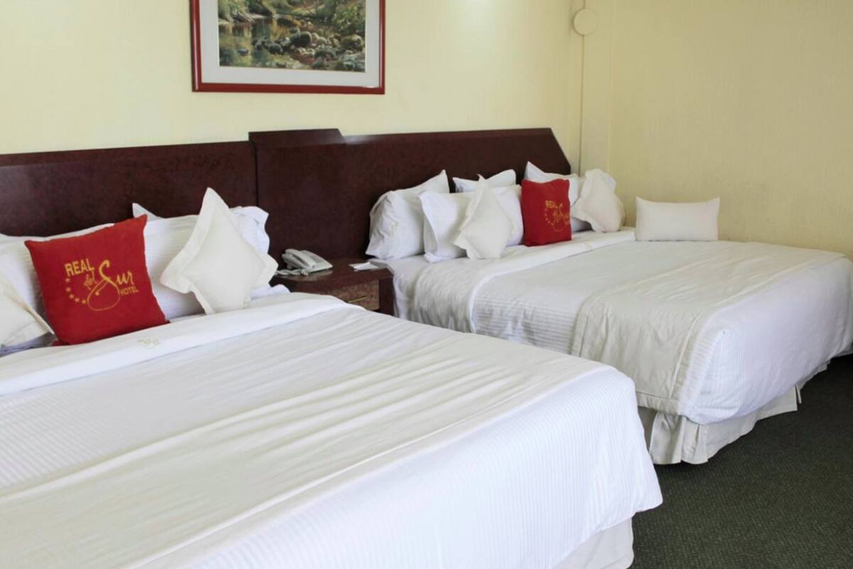 Two single beds with white linens, a wooden headboard, a telephone on the nightstand, and a framed picture on the wall.