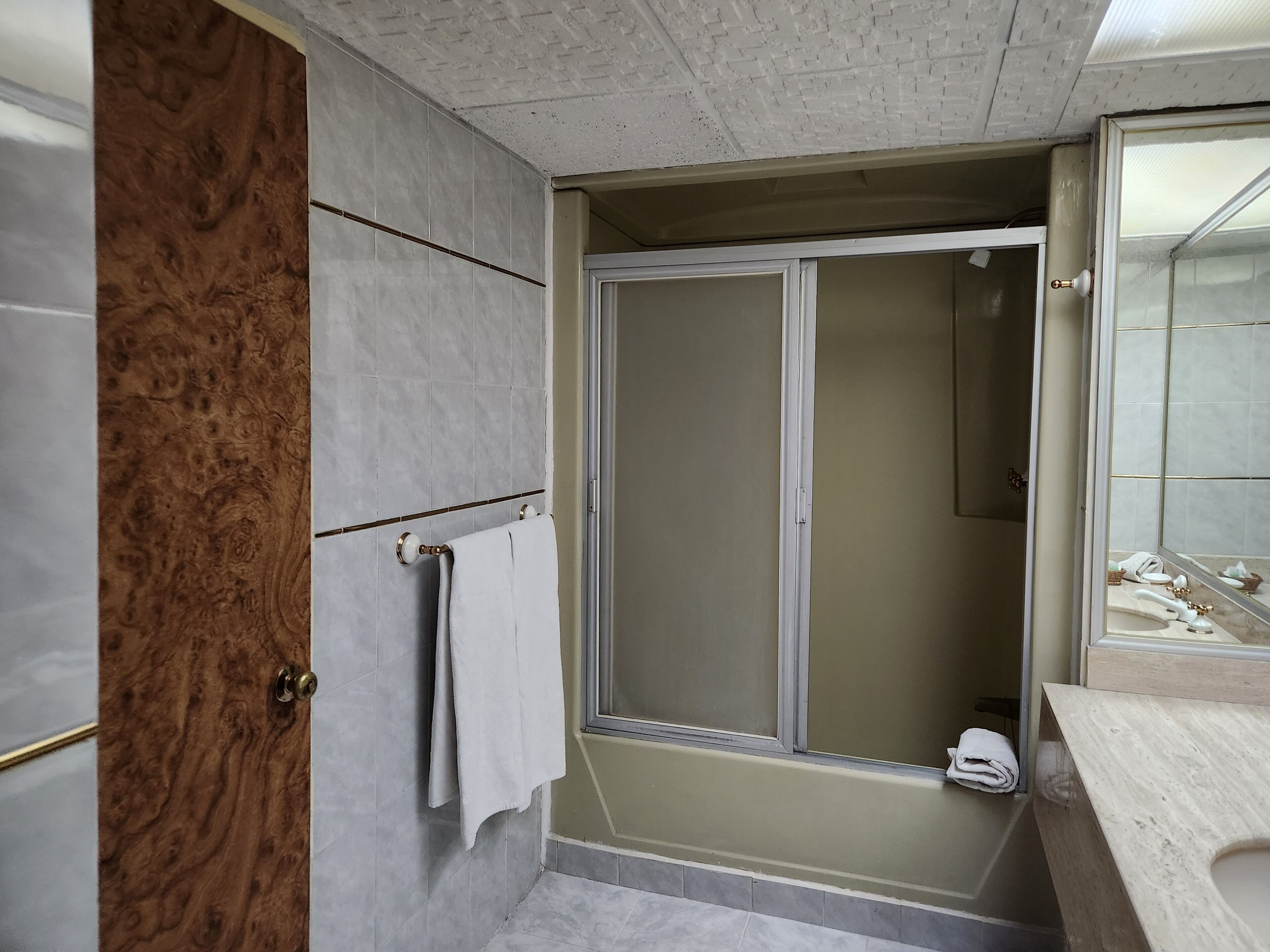 A bathroom with a wooden door, a towel rack, a shower with a glass door, and a mirror.