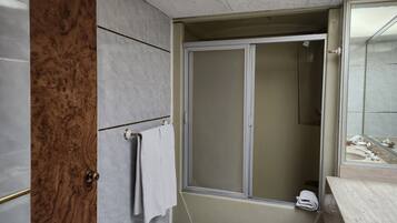 A bathroom with a wooden door, a towel rack, a shower with a glass door, and a mirror.