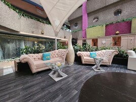 Un hall d’entrée spacieux, agrémenté de deux canapés confortables, d’une table basse en verre et d’un grand vase décoratif. L’espace est doté d’un mur en pierre orné de plantes vertes, d’une cascade et d’un éclairage combinant des sources naturelles et artificielles.