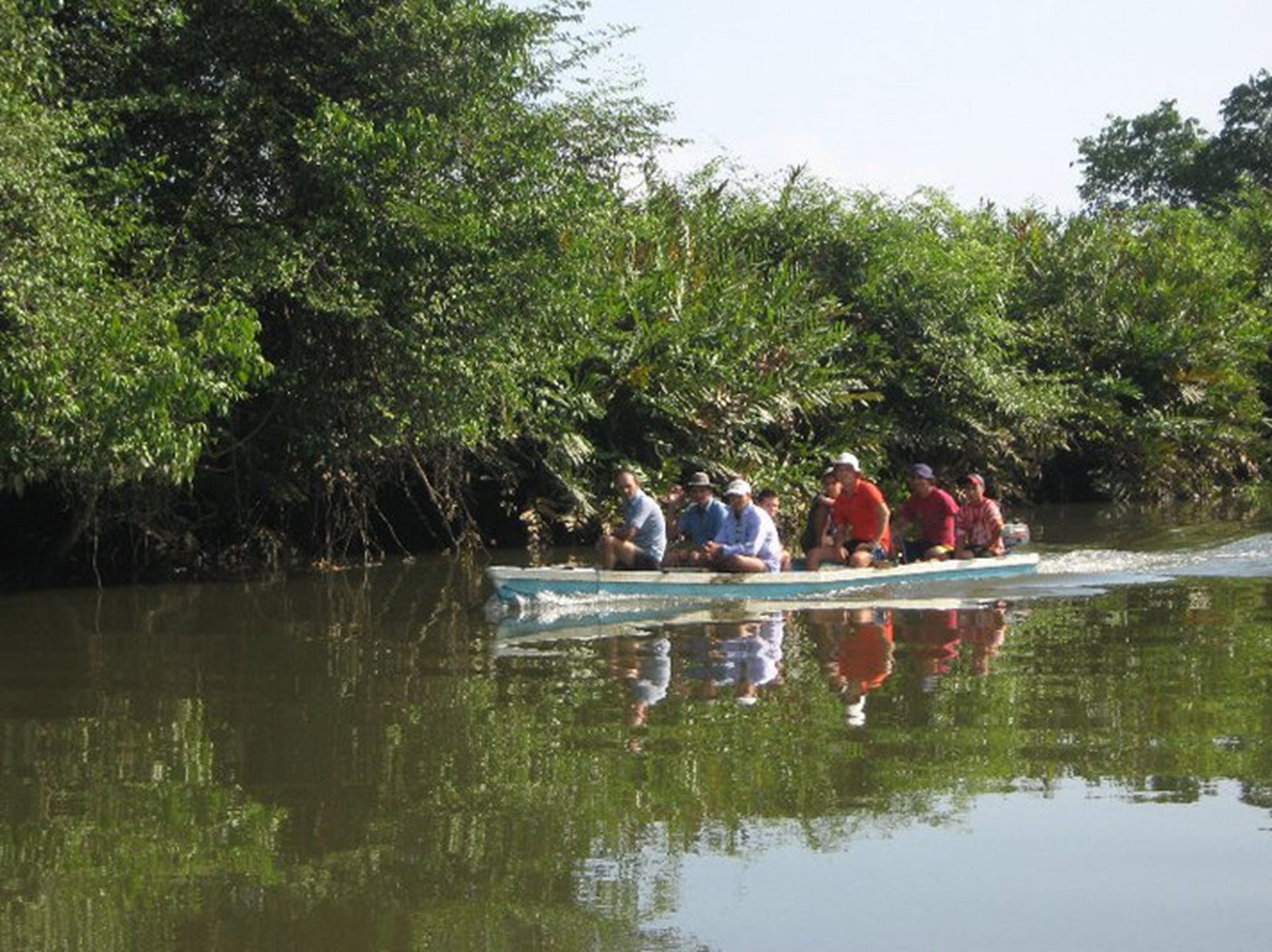 Un grup de persones en una barca surant en un riu tranquil envoltat de vegetació abundant.