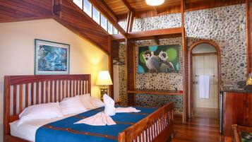 A wooden-framed bed with a blue bedspread and white pillows, a stone wall with a monkey painting, and a wooden ceiling with exposed beams.