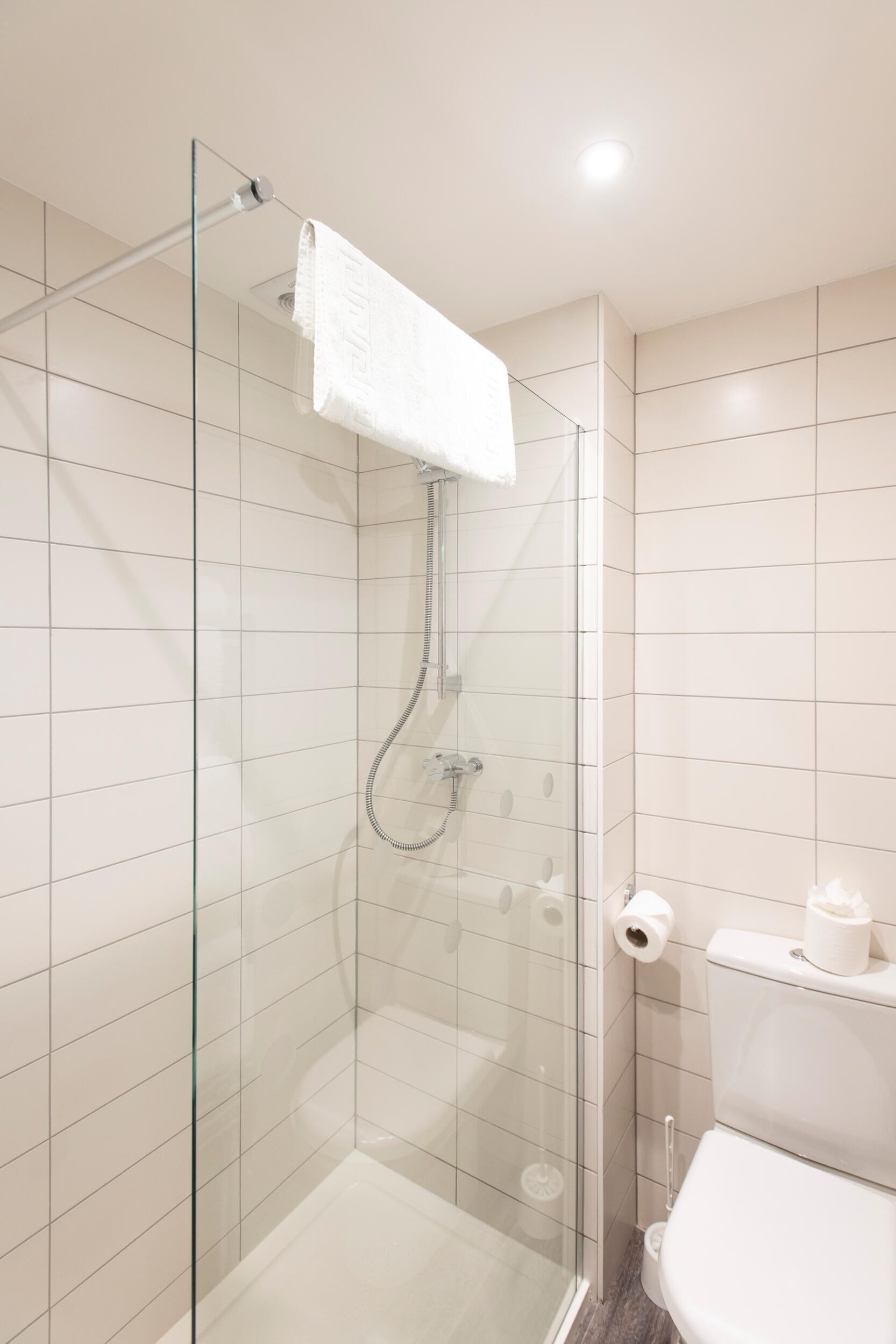 Un baño moderno con ducha envuelta en vidrio, azulejos blancos y un inodoro con dispensador de toallas de papel.